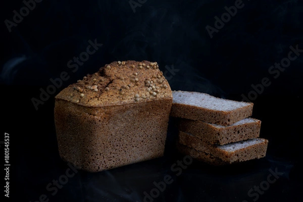 Fototapeta Half a loaf and pieces of sliced buckwheat bread on a black background.