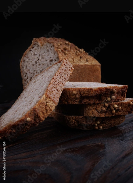 Fototapeta Half a loaf and pieces of sliced buckwheat bread on a dark wooden background.