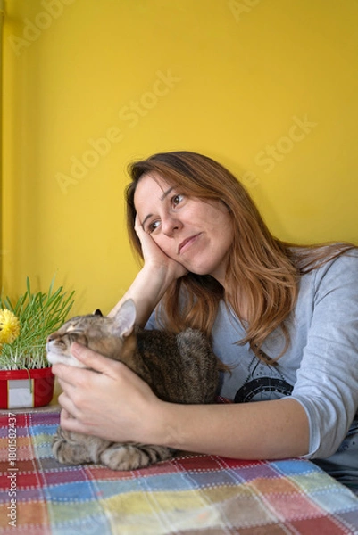 Fototapeta A woman with her cat friend at the table in the morning