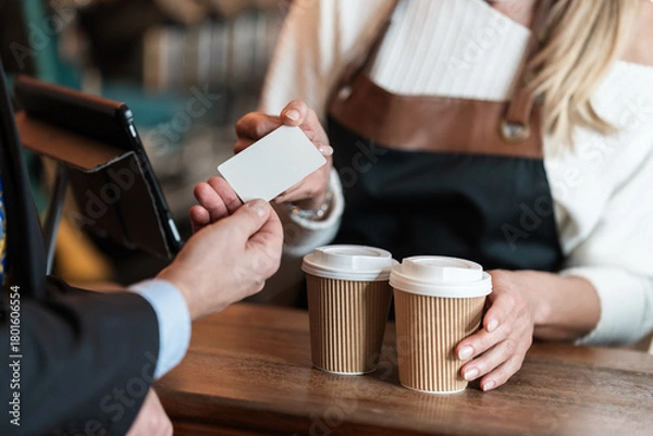 Fototapeta A businessman pays by card for his takeaway coffee while the cafe barista processes the customer credit card with friendly service
