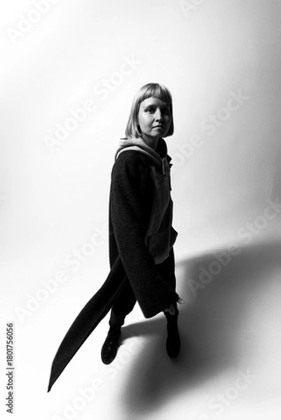 Fototapeta A model strikes a confident pose in a modern outfit, showcasing a blend of black and gray hues. The minimalist background highlights her presence at an indoor studio setting