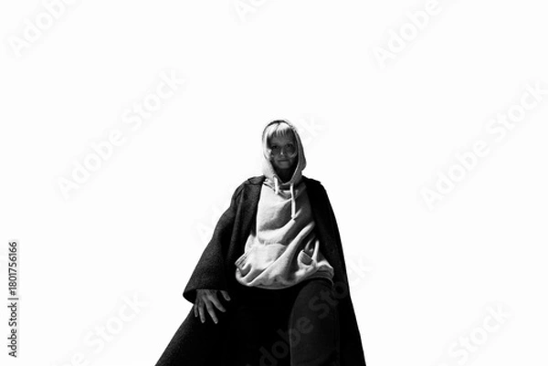 Fototapeta A person dressed in a cozy hoodie and a flowing cloak stands tall, exuding confidence. The simple background emphasizes their unique style and expression, inviting curiosity about their story