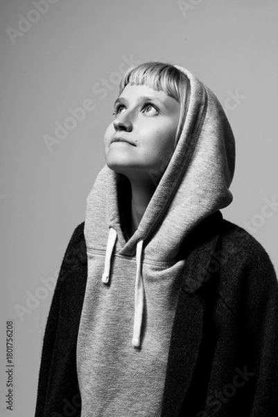 Fototapeta Soft natural light illuminates a young person gazing upward with a hopeful expression. Dressed in a snug hoodie and a coat, they embody a moment of introspection and aspiration