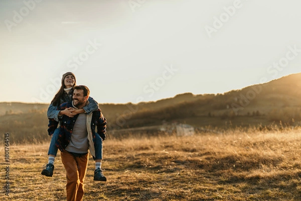 Obraz Smiling couple piggybacking in nature during sunset