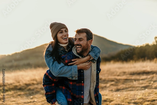 Obraz Happy couple enjoying piggyback ride in nature at sunset