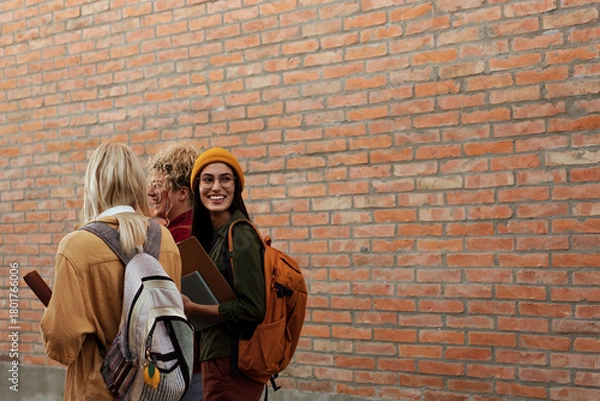 Obraz College students walking by brick wall smiling