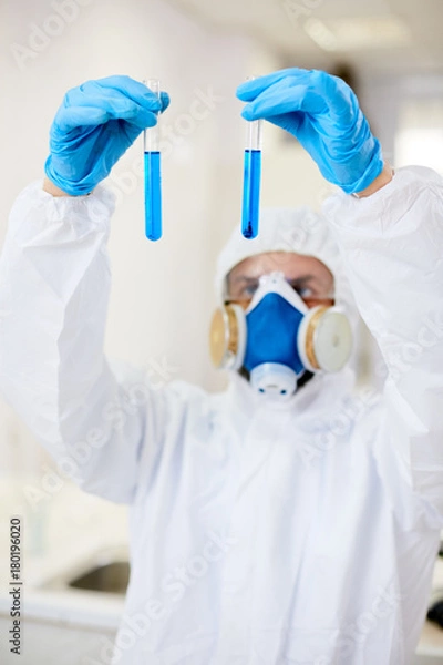 Fototapeta Gloved scientist holding two flasks with blue liquids