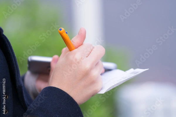 Obraz メモを取りながらスマートフォンを使う女性