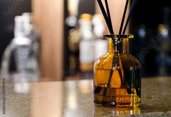 Fototapeta Stylish amber glass aroma diffuser with black reeds stands on a polished bar counter.