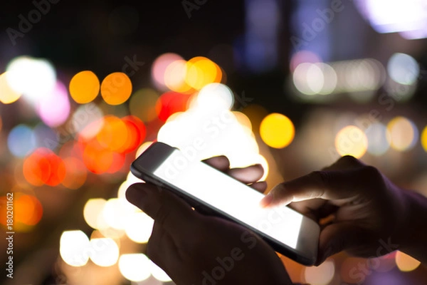 Fototapeta Two hands of man playing smartphone with bright white monitor on colorful bokeh background for hi technology concept that look like advance
