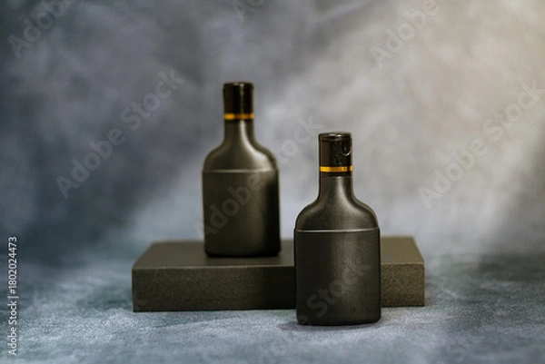 Fototapeta Two elegant black cosmetic bottles standing against a textured gray background. This minimalist mockup is perfect for branding, product packaging previews, advertising materials, and modern design