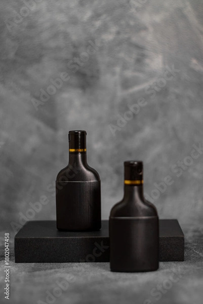 Fototapeta Two elegant black cosmetic bottles standing against a textured gray background. This minimalist mockup is perfect for branding, product packaging previews, advertising materials, and modern design