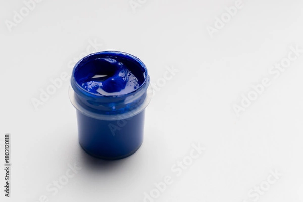 Obraz A jar of colored blue gouache on a white background. Copy space. A transparent jar of colored water-soluble paint.