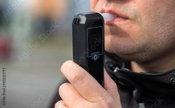 Fototapeta Male Driver Using Personal Alcometer For Sobriety Check. Man Exhaling Into Alcohol Test Device. Driving license revocation for alcohol