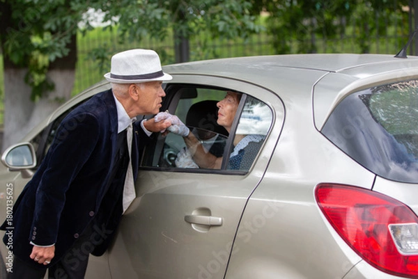 Fototapeta Elderly couple shares a heartfelt moment by a parked car during a sunny afternoon