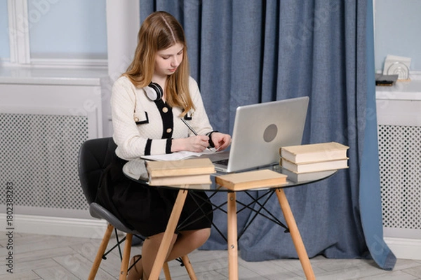 Fototapeta Female professional working remotely, sitting in living room. Woman working diligently at desk with laptop in home office, in cozy setting surrounded by books, preparing for presentation, seminar