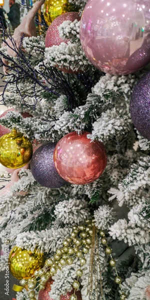 Fototapeta Festive Christmas tree decorated with pink, gold, and purple baubles on snowy pine branches creating a cozy holiday mood. Selective focus