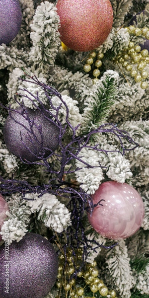 Fototapeta Festive Christmas tree decorated with pink, gold, and purple baubles on snowy pine branches creating a cozy holiday mood. Selective focus