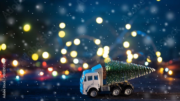 Fototapeta A toy truck transports a Christmas tree. Blue bokeh background with garland and falling snow.
