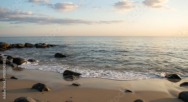 Obraz Golden Hour Serenity - Gentle Waves on a Rocky Beach Under a Soft Sky.