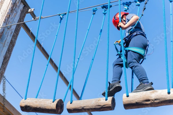 Fototapeta Child boy in Protective Gear Navigating a High Ropes Course in adventure park 
