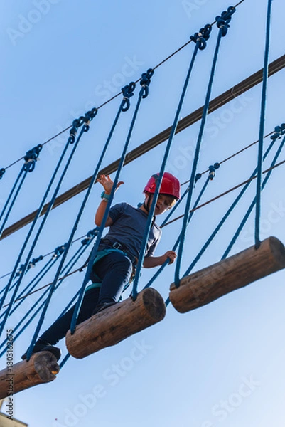 Fototapeta Child boy in Protective Gear Navigating a High Ropes Course in adventure park 