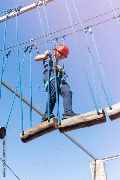 Fototapeta Child boy in Protective Gear Navigating a High Ropes Course in adventure park 