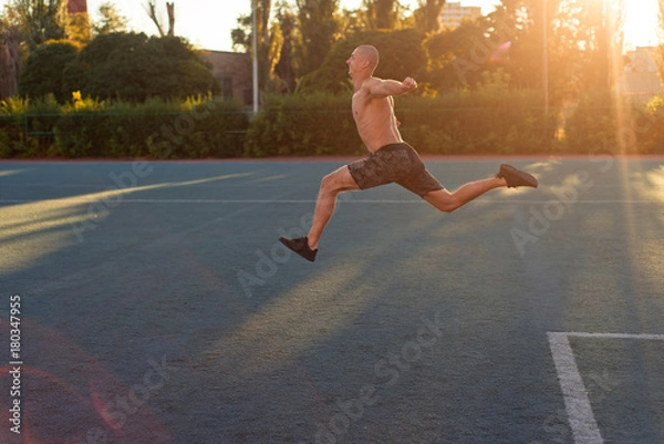 Fototapeta A man athlete starts to run, jumps in the stadium
