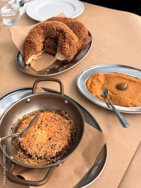 Obraz traditional greek food on table with round stone baked bread with sesame seeds and spicy dip served on table with brown paper tablecloth