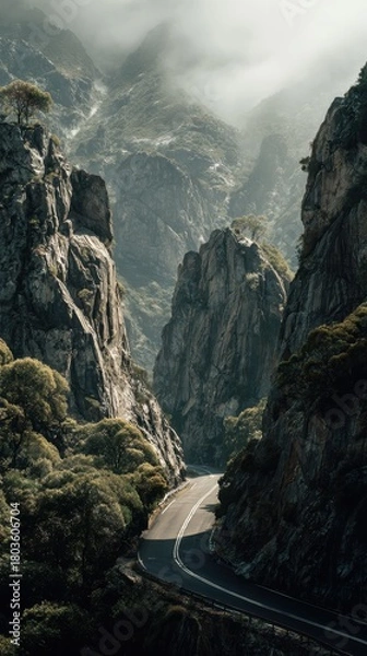Obraz Dramatic Mountain Pass Road Winding Through Rugged Peaks Under Ethereal Misty Sunlight.