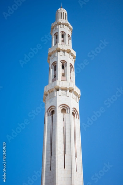 Fototapeta A tall, elegant white mosque minaret rising against a bright blue sky. The tower features arched windows, subtle geometric detailing, and traditional Islamic architectural elements