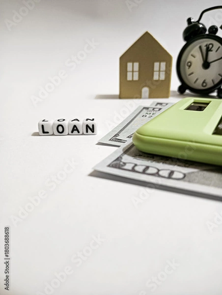 Fototapeta A conceptual image showing a house model, alarm clock, cash, calculator, and dice spelling “LOAN,” symbolizing mortgage planning, financial deadlines, and budgeting for home financing.