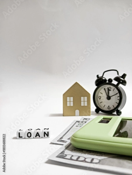 Fototapeta A conceptual image showing a house model, alarm clock, cash, calculator, and dice spelling “LOAN,” symbolizing mortgage planning, financial deadlines, and budgeting for home financing.