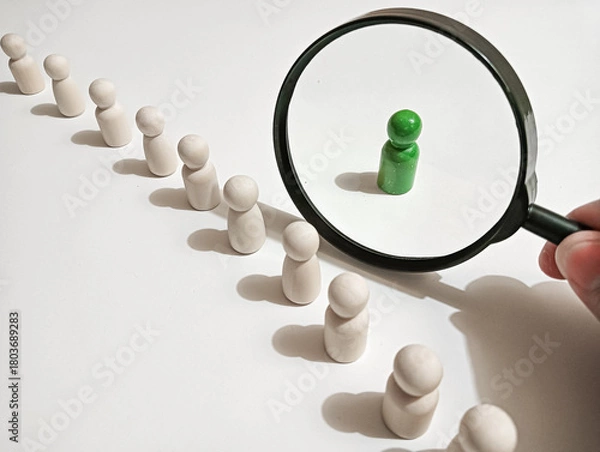 Fototapeta A single green figure stands apart from a line of natural wooden figures, symbolizing uniqueness, individuality, leadership, and distinction in a minimal conceptual setup.