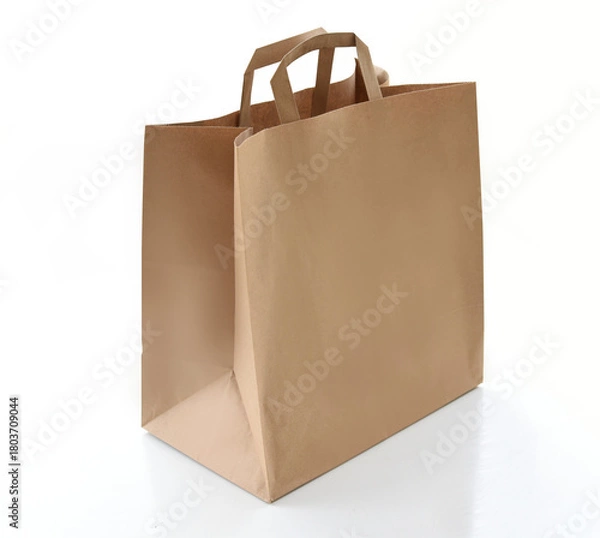 Obraz Plain kraft paper shopping bag with handles on a clean white background. Eco-friendly packaging concept for retail, delivery, gifts, or branding. Minimalistic studio shot of a reusable paper bag.