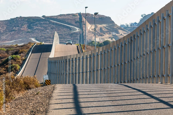 Fototapeta Międzynarodowy mur graniczny między San Diego w Kalifornii i Tijuaną w Meksyku, z nadjeżdżającym pojazdem Straży Granicznej na pobliskim wzgórzu.