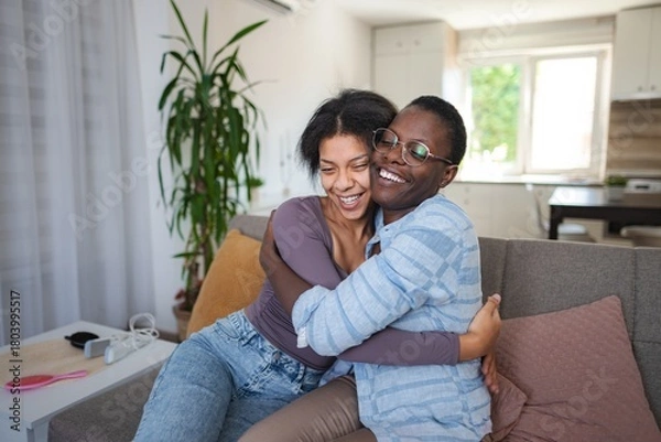 Fototapeta Two joyful friends hugging and laughing on the sofa at home