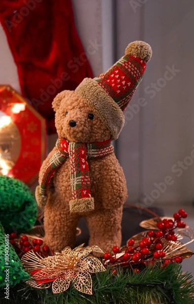 Fototapeta Christmas interior with vintage teddy bear figurine in a plaid Santa hat on the background of a red stocking for gifts and on a green blanket with gold stars as an interior decoration concept 