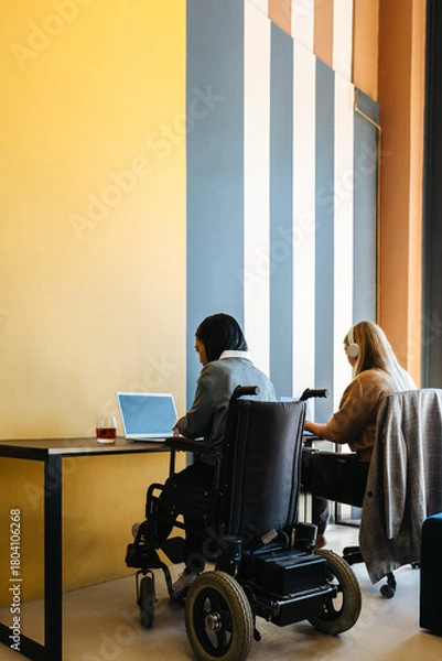Obraz Two young women working together at a shared desk in an office