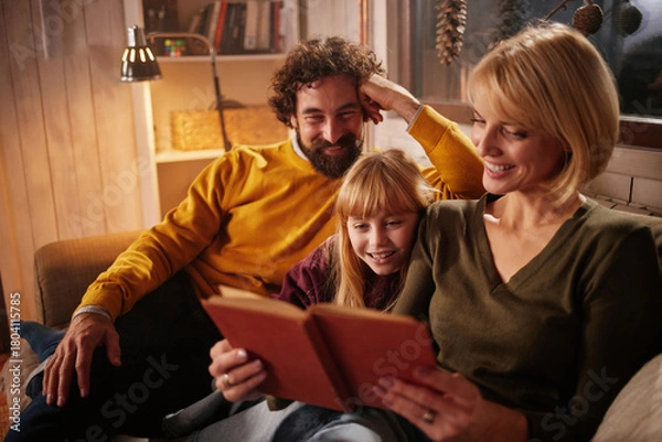 Obraz In a warm, inviting living room, a family sits together on a couch, enjoying a book. The atmosphere is cozy as they share laughter and moments of joy, creating lasting memories.