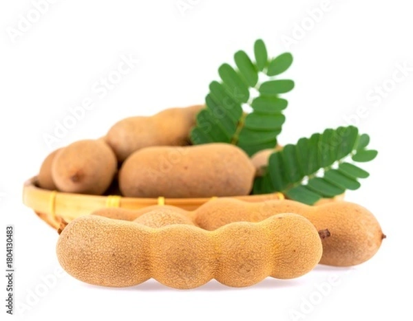 Fototapeta Ripe tamarind pods displayed in a woven basket with green leaves on white