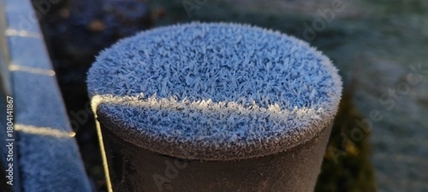 Fototapeta A close-up of hoar frost covering a fence post on a cold winter morning. Detailed macro texture of ice crystals sparkling in the golden sunlight