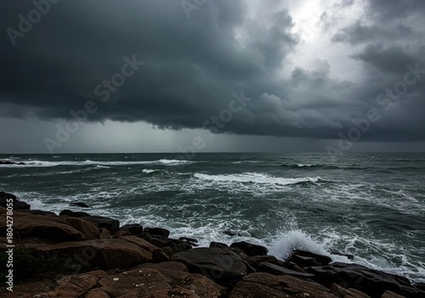 Fototapeta Dramatic, stormy seascape featuring dark, heavy clouds covering the sky over a churning gray ocean with rough waves crashing against a rugged shoreline ,foam ,turbulent ,somber
