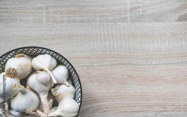 Fototapeta Top view of garlic in a black and white glass bowl on a wooden neutral background, top view
