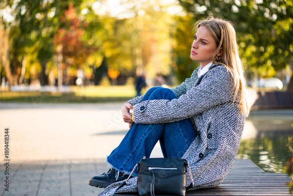 Fototapeta Portrait of sad businesswoman sitting alone on a park bench in the city during autumn day.