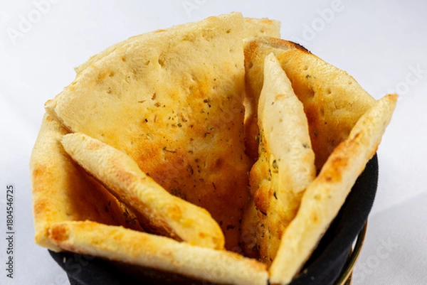 Fototapeta Foccacia or pita. Triangular pieces of lightly browned Pita, Naan, or flatbread served in a black fabric basket on a white background.