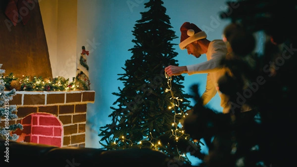 Fototapeta Man Decorates Christmas Tree While Dancing with White LED Lights