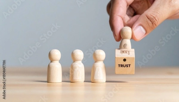 Fototapeta Four wooden figurines on wood surface, one lifted onto “TRUST” block with keyhole symbol.
