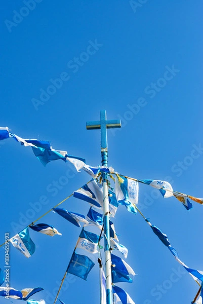 Obraz A striking blue cross, covered in glittering material, stands tall against a clear blue sky, surrounded by blue and white prayer flags.