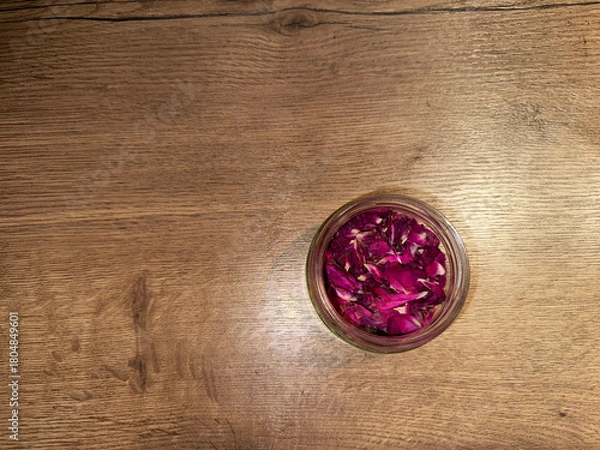 Fototapeta Glass jar with tea rose petals on a wooden surface, top view, soft light, copy space. Elegant, minimalistic background for spa, wellness designs, cooking themes, herbal cosmetics, self-care projects